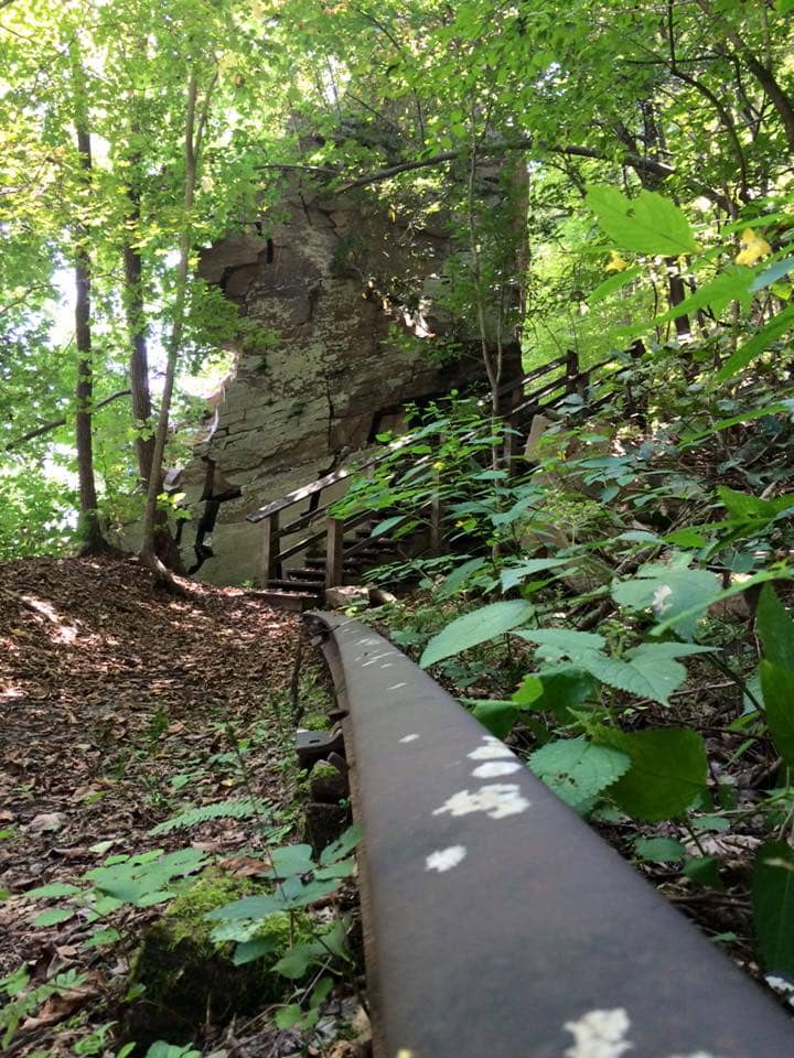 An old railroad line in the foreground leads to a wooden staircase that wraps around an enormous bolder in the middle of the Rend Trail. 