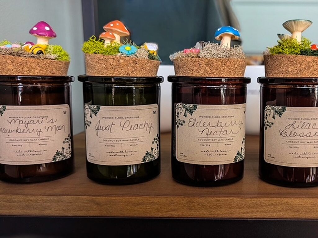 Four jar candles with cork tops that appear to have grass, moss and mushrooms growing on top.