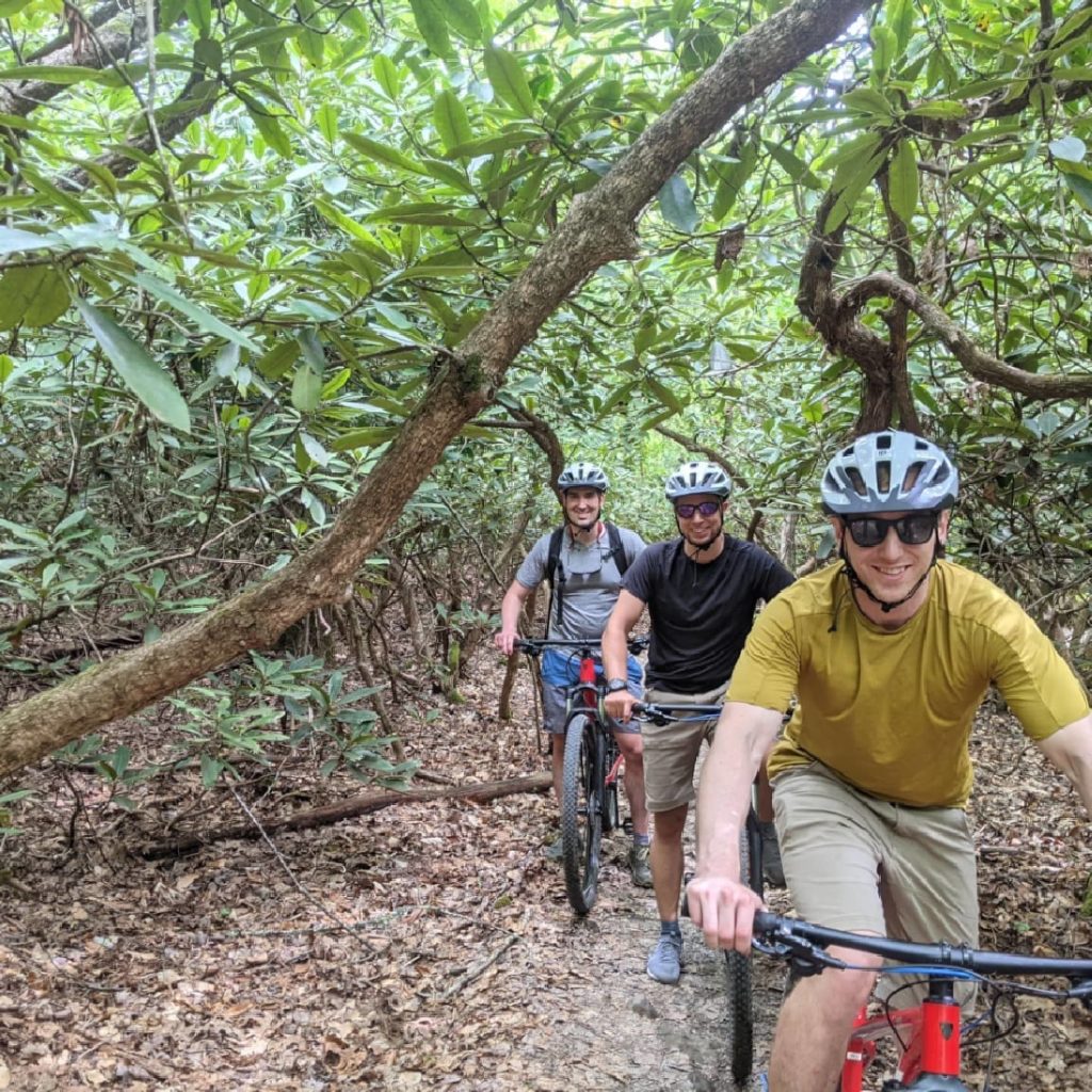 Three men on mountain bikes going through the rhododendran tunnels that are found on many trails in the New River Gorge National Park.