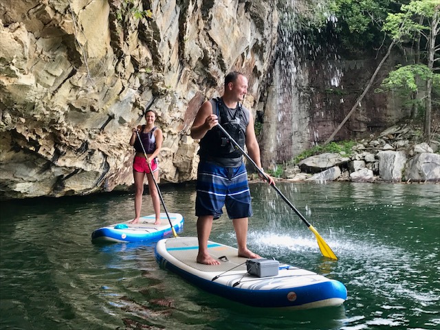 A coulple standup paddleboarding under a waterfall in New River Gorge.