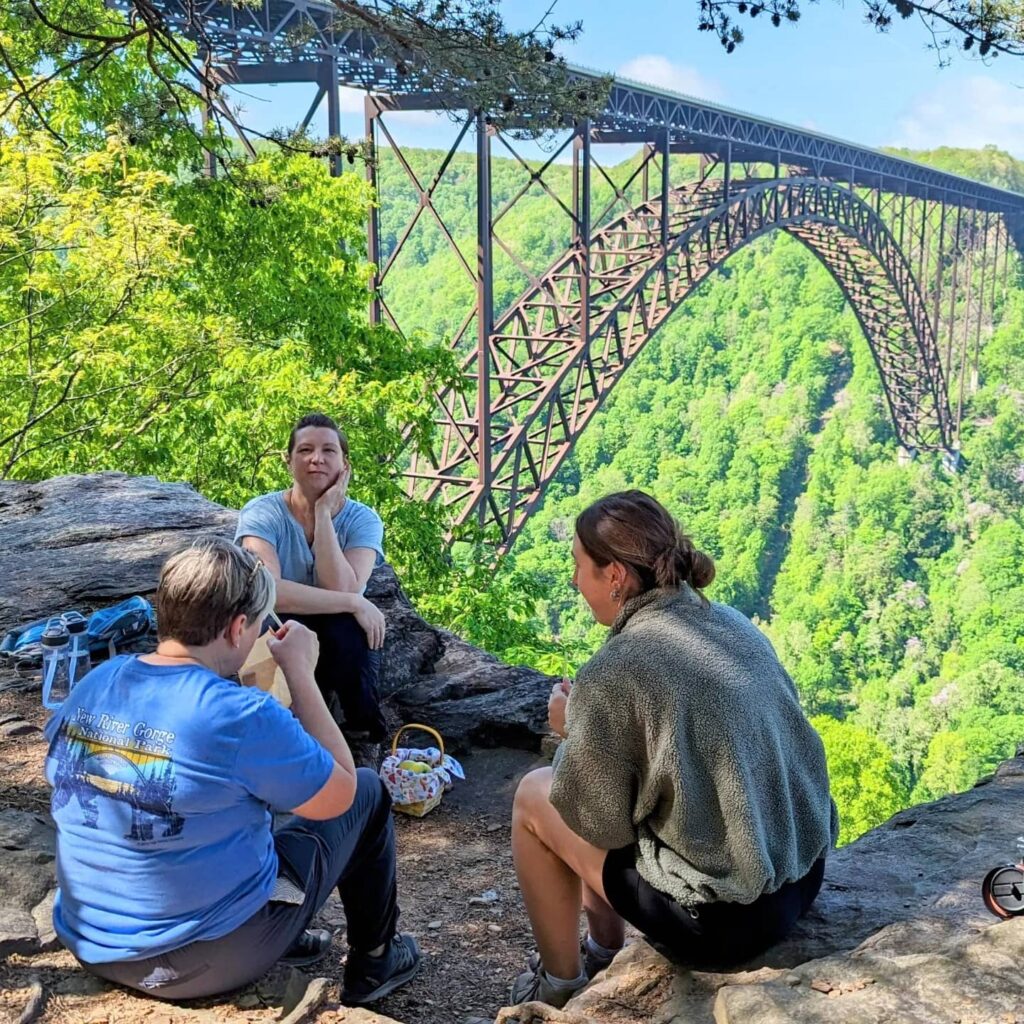 Two New River Gorge Eco Tour guests sitting with Amy of Lafayette Flats by the New River Gorge Bridge.