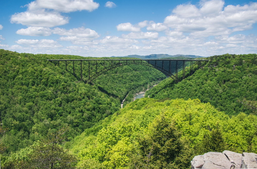 The New River Gorge Bridge stretching between to green, tree-covered mountains with the blue river below. 