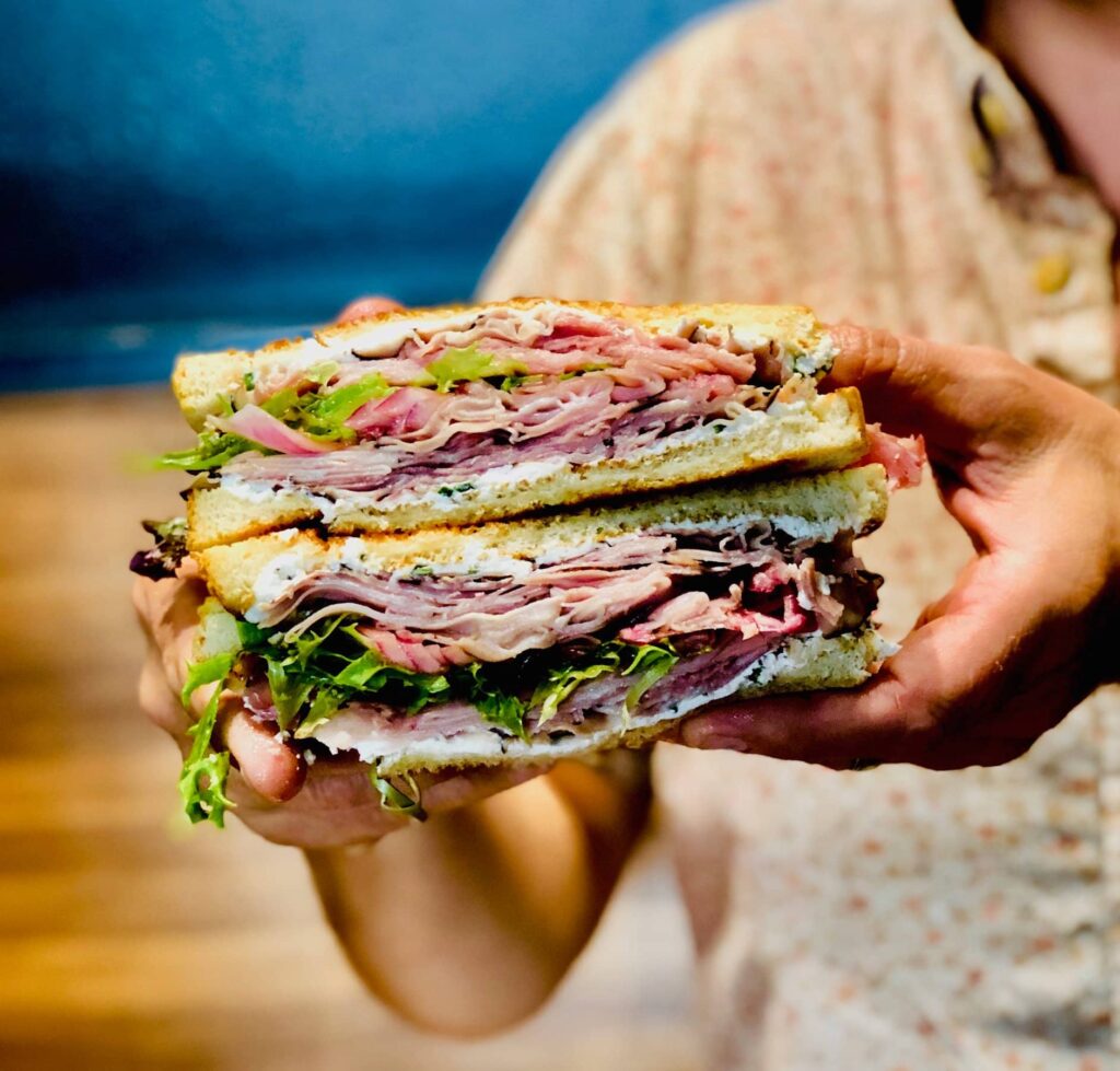 A huge Secret Sandwich Society sandwich cut in half with lots of meat, cheese and condiments.