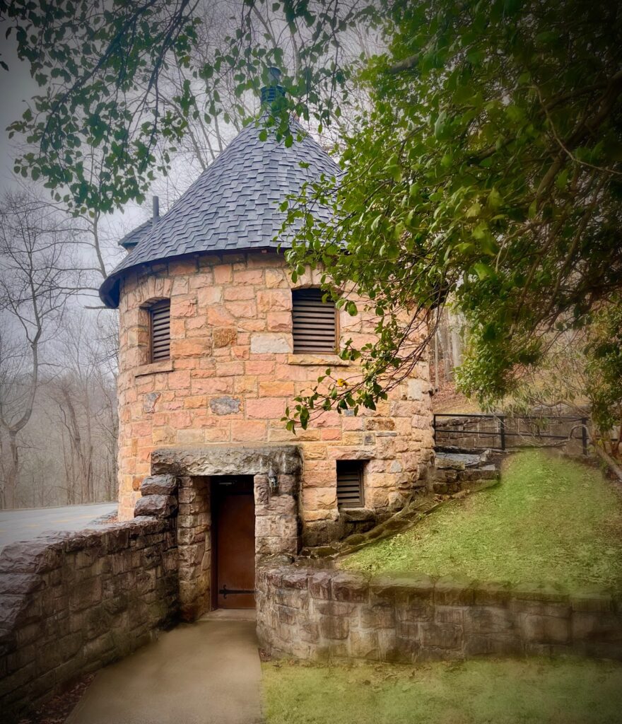 A turret shaped building made from pink Nuttall sandstone with a grey shingled roof. The bathroom at Hawks Nest State Park Main Overlook.