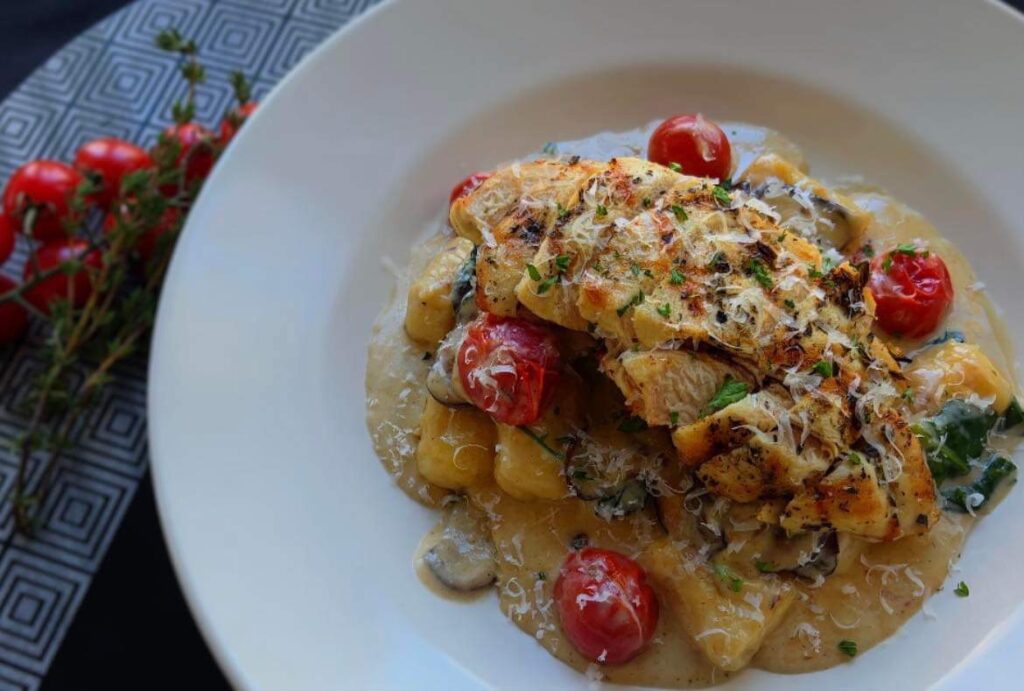 Seasoned chicken with red tomatoes in a white plate at the Gaines Estate. 