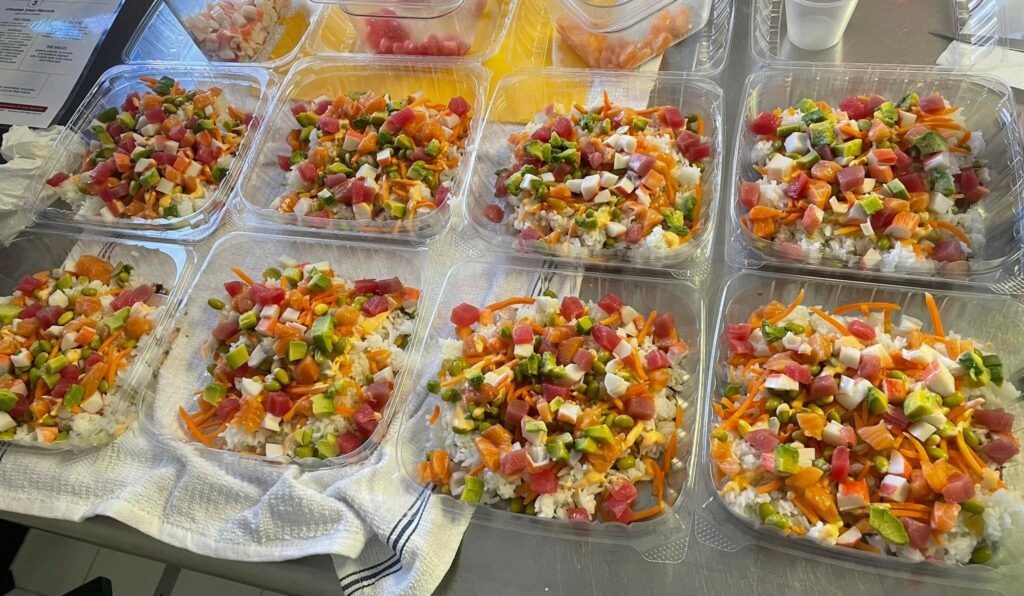 Rows of colorful sushi bowls in to-go containers lined up on a counter at the Take Out. 