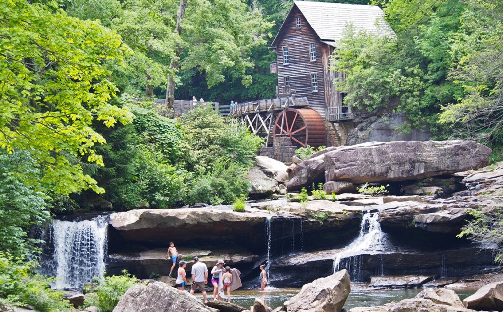 A family playing and swimming in the water hole below the old grist mill at Babcock State Park. There are big rocks and waterfalls all around them. 