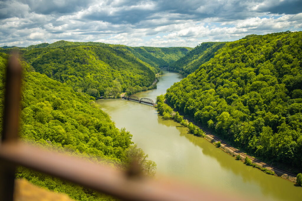 Looking down on green West Virginia hills and the New River from the Hawks Nest Overlook. The railroad bridge across Hawks Nest Lake is present in the distance. 