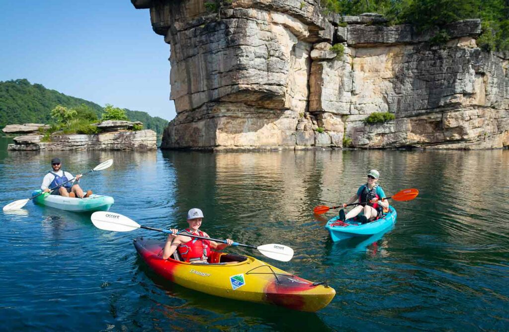 A mom in a blue kayak, a dad in a light blue kayak, and a son in a yellow kayak in PFDs on Summersville Lake in the New River Gorge. 